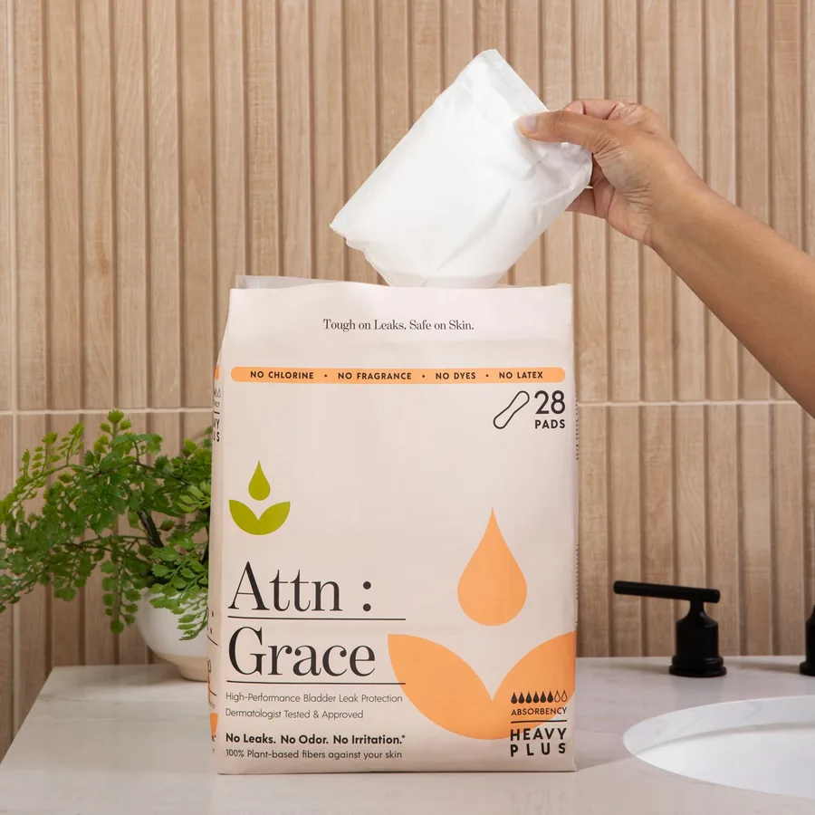 A hand holding an open Attn: Grace pad beside the pack